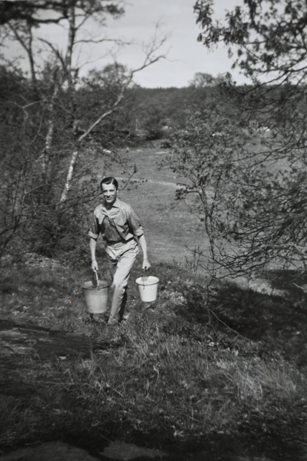 Mitten på 1950-talet: Leif Kondrup på väg till stugan ovanför kullen med vatten från pumpen på ängen; i bakgrunden syns ängen där grillplatsen finns nu.